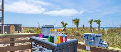 Un quiosco en la playa con un refrigerador, botellas de bebidas de colores y un calentador portátil.