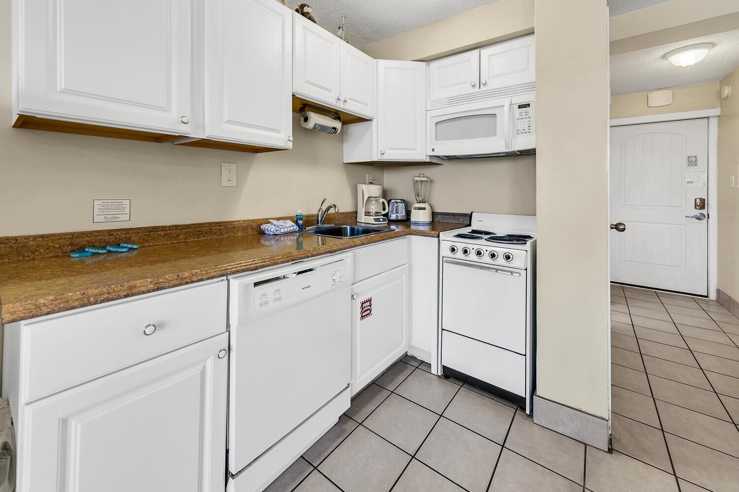 A compact kitchen with white cabinetry, a microwave, a stove, and a dishwasher.