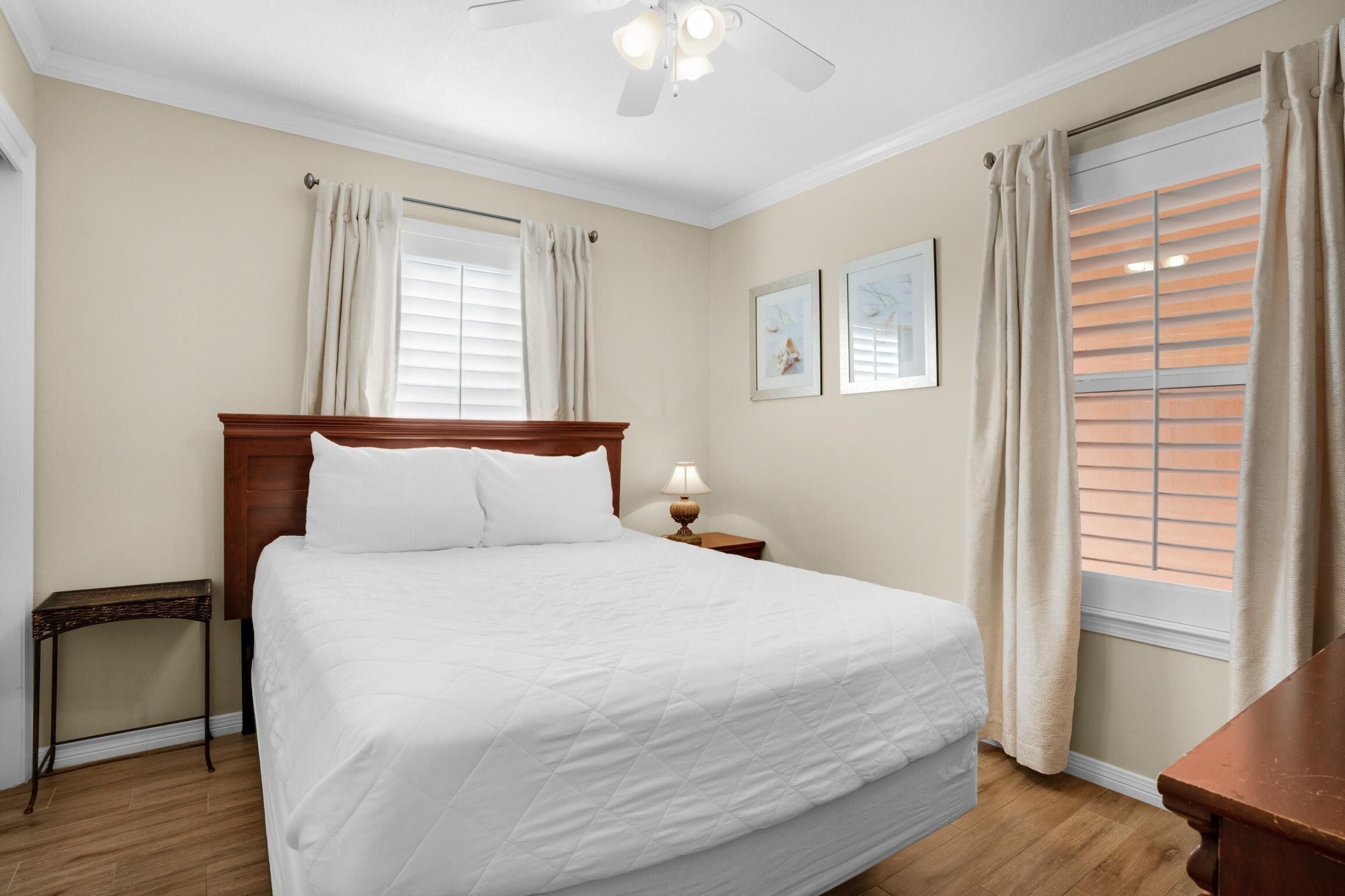 Een net opgemaakt bed in een hotelkamer, met een houten hoofdbord, een nachtkastje met een lamp en een raam met zonwering.
