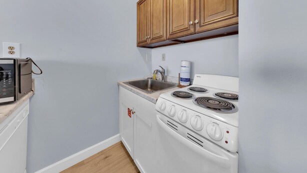 A compact kitchen with a white stove, wooden cabinets, and a sink. - Top of the Gulf 416 (Panama City Beach)