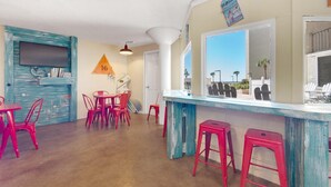 A room with a bar area, red chairs, a large window, and a view of palm trees. - Top of the Gulf 416 (Panama City Beach)