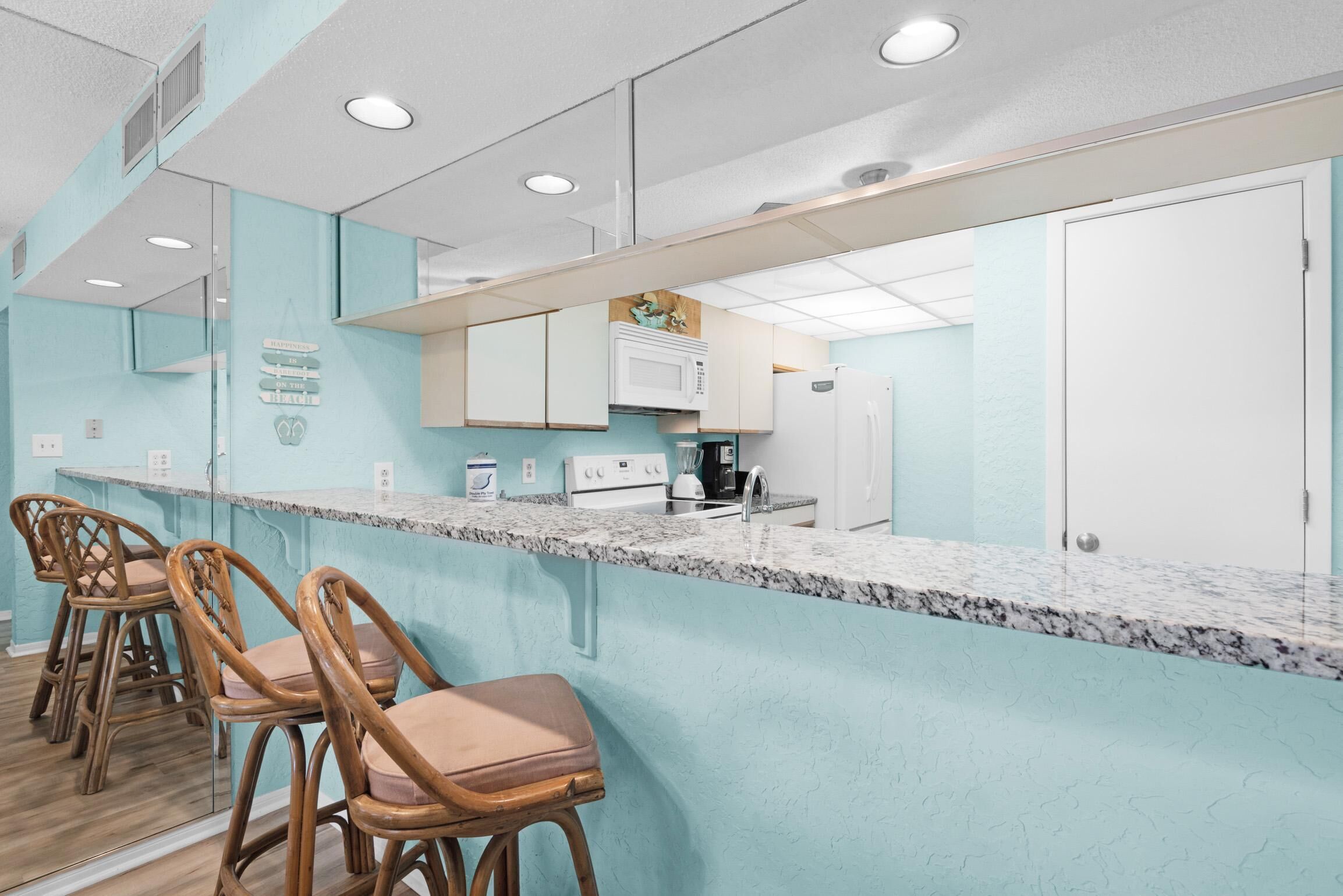 A kitchen with a marble countertop, wooden chairs, and a white refrigerator.