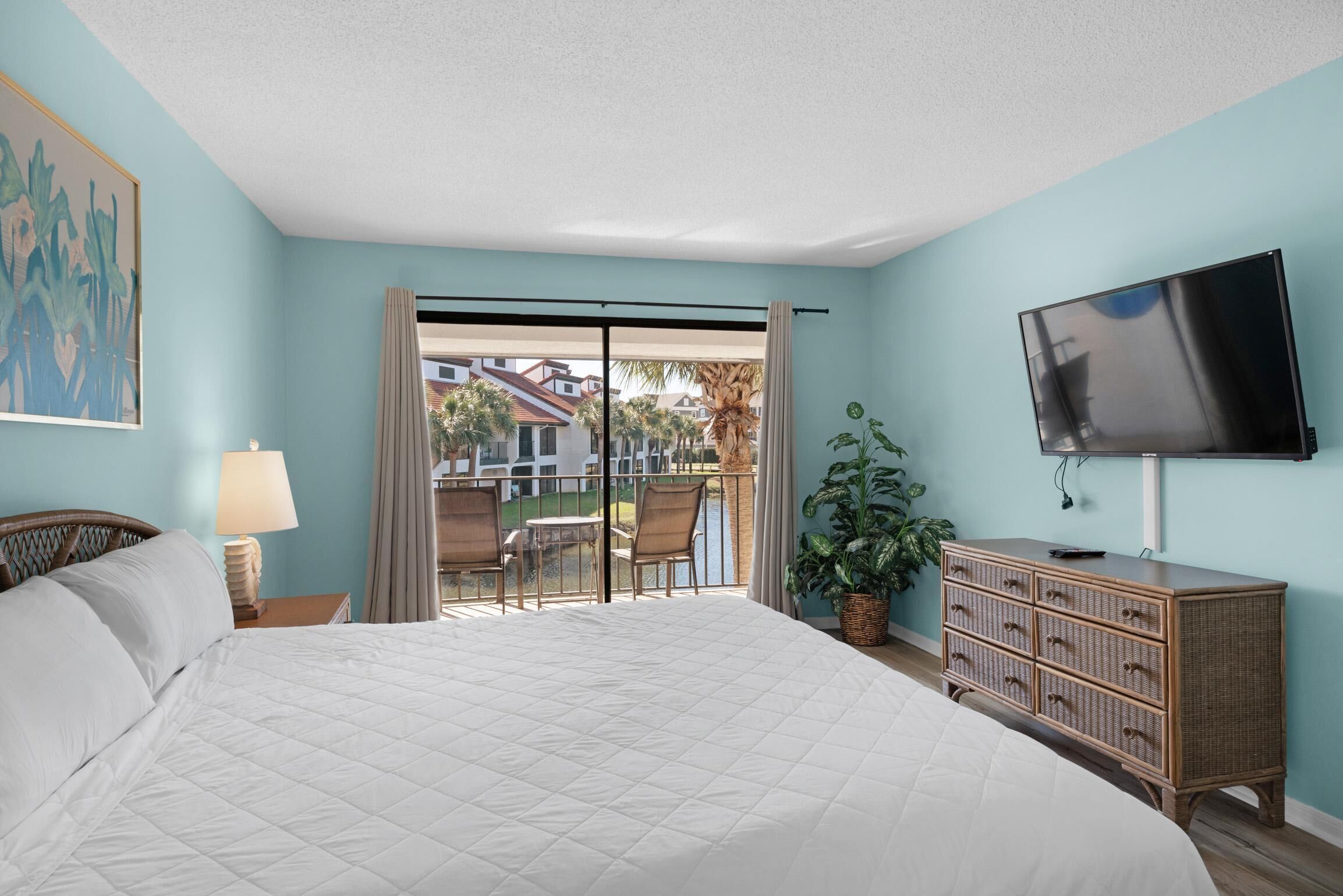 A bedroom with a large bed, a television, a dresser, and a balcony with outdoor seating.