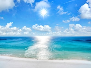 A beach with clear turquoise waters and a bright sun shining over it. - Majestic Beach Towers 1-1701 (Panama City Beach)
