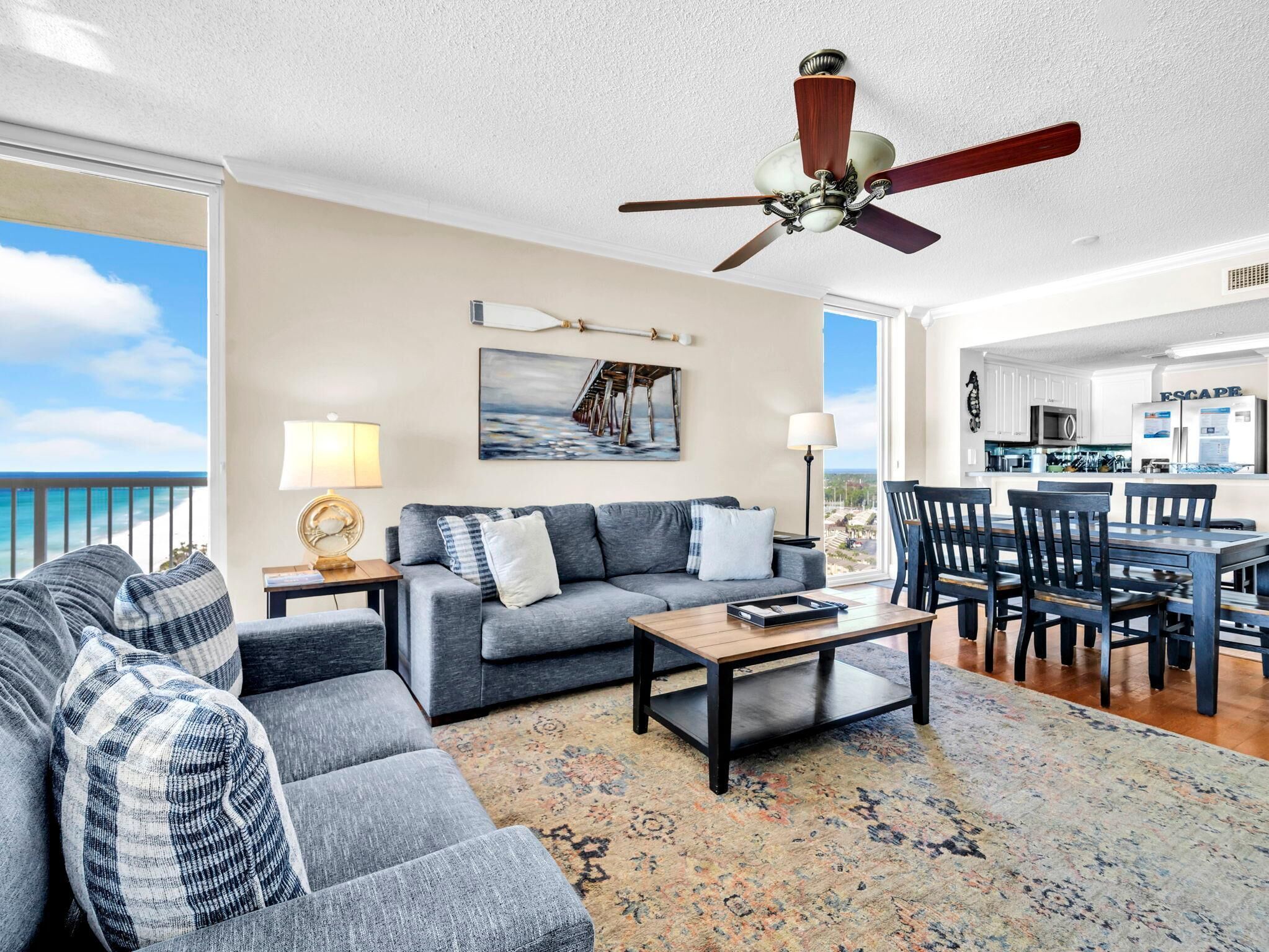 A spacious living room with a grey sofa, a coffee table, and a view of the ocean through large windows.