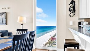 Quarto com vista para a praia e oceano, área de refeições com mesa e cadeiras, e cozinha decorada com um enfeite de cavalo-marinho.