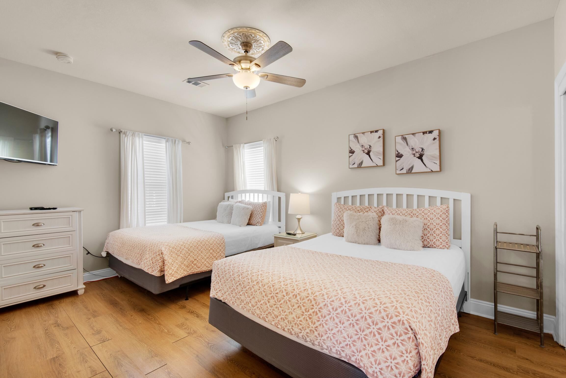 A bedroom with two beds, a ceiling fan, a dresser, and artwork on the wall.