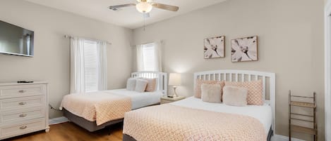 A bedroom with two beds, a ceiling fan, a dresser, and artwork on the wall.