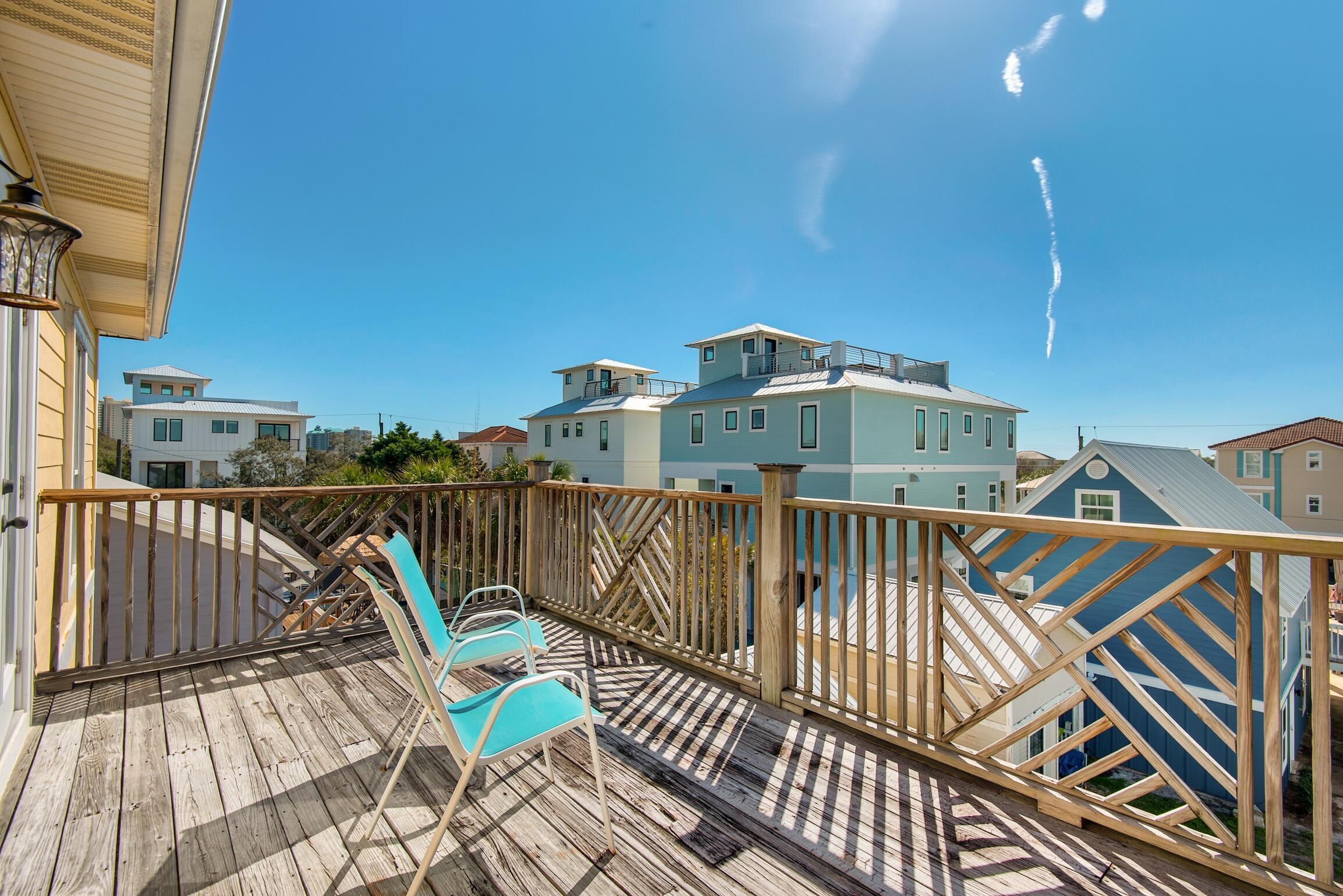 A wooden deck with two blue chairs, a railing, and a view of neighboring houses.