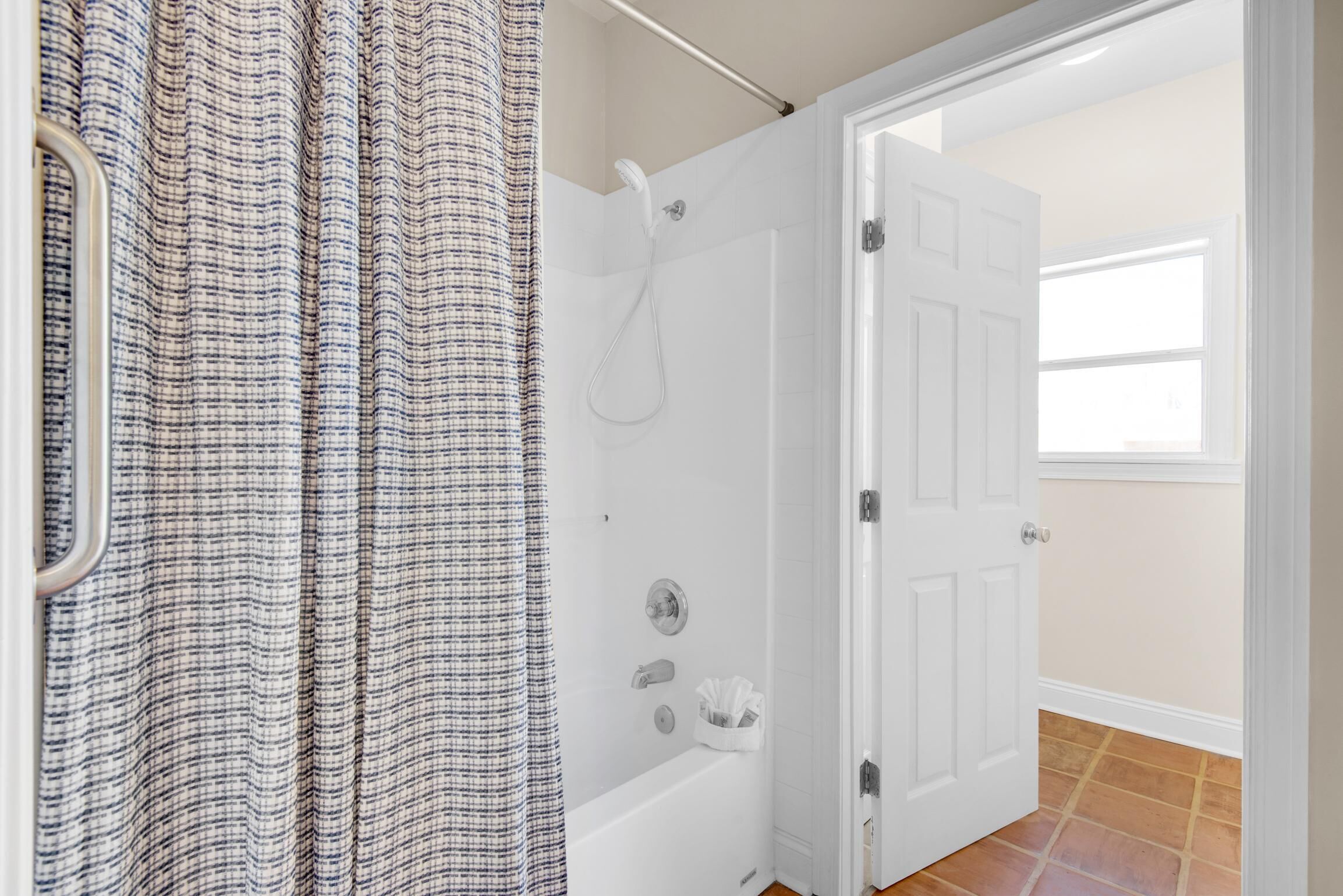 Een badkamer met een douche, een witte deur en een raam.