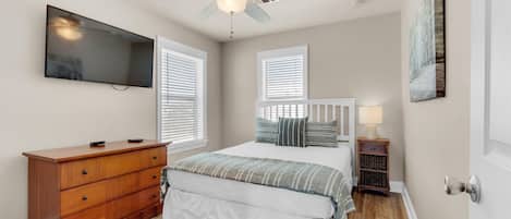 A bedroom with a bed, dresser, ceiling fan, TV, and artwork.