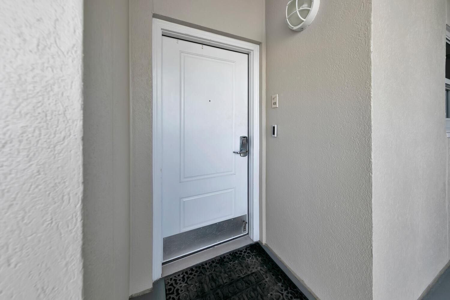 A white door with a keypad lock, a small step leading to the door, and a wall-mounted light fixture.