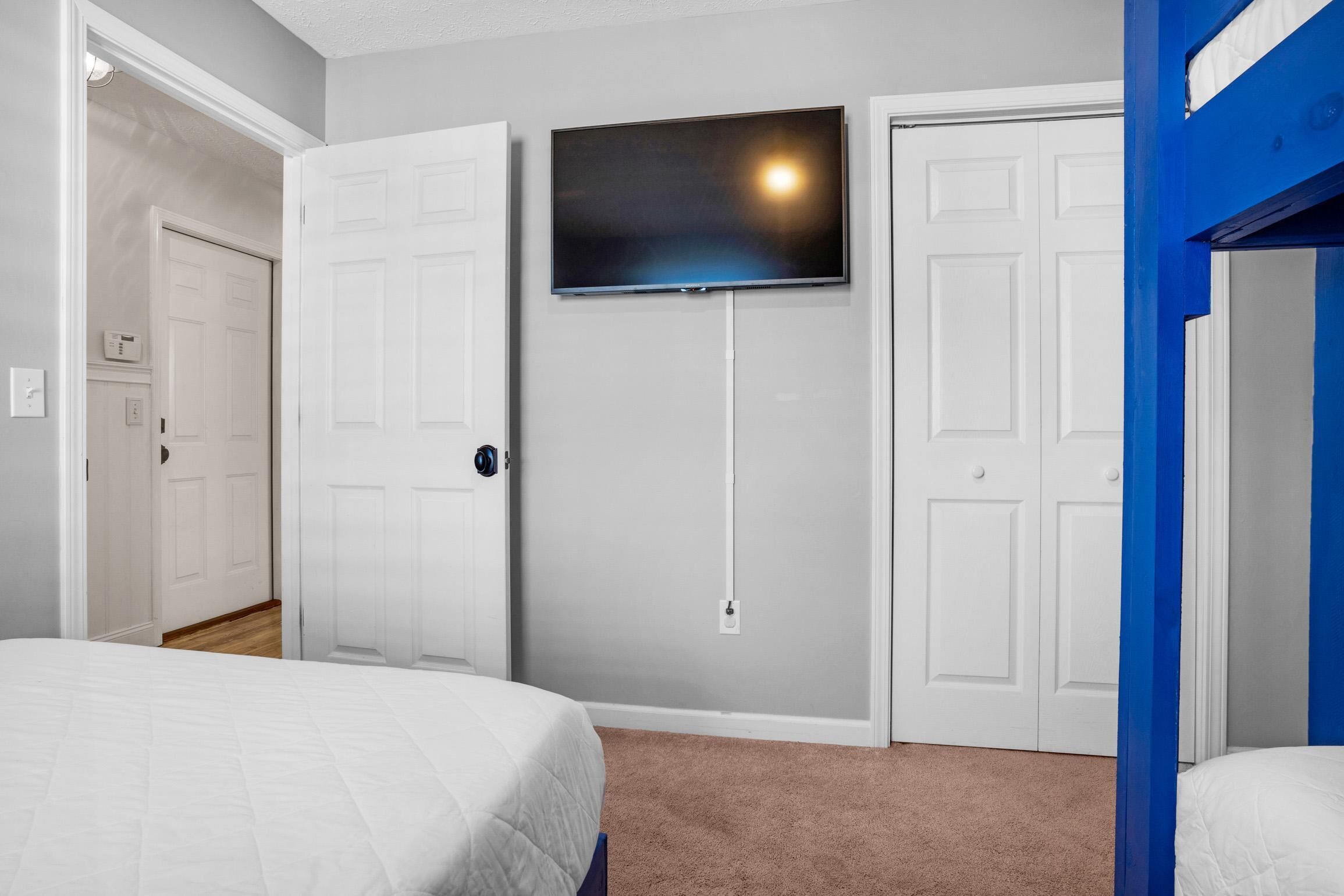 A bedroom with a bed, a TV mounted on the wall, and two white doors.