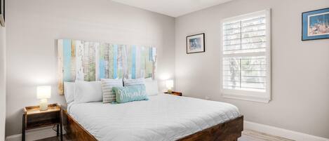 Une chambre à coucher avec un lit en bois, un ventilateur de plafond, une fenêtre avec des stores et un tableau accroché au mur.