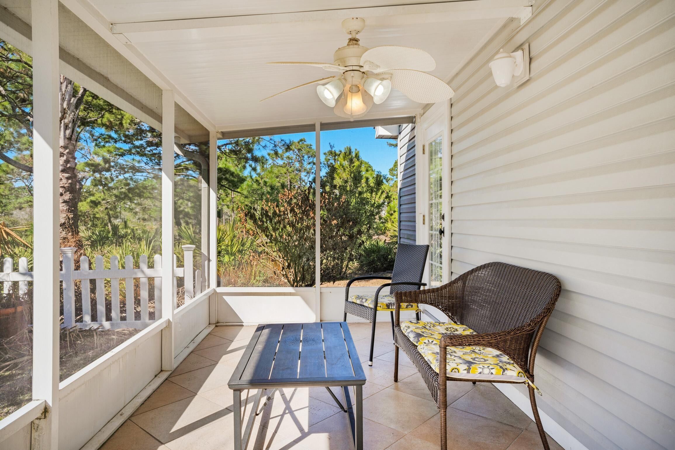 A covered patio with a table and chairs, a ceiling fan, and a view of trees and vegetation.