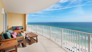 A balcony with a view of the beach, wooden furniture, and a railing.