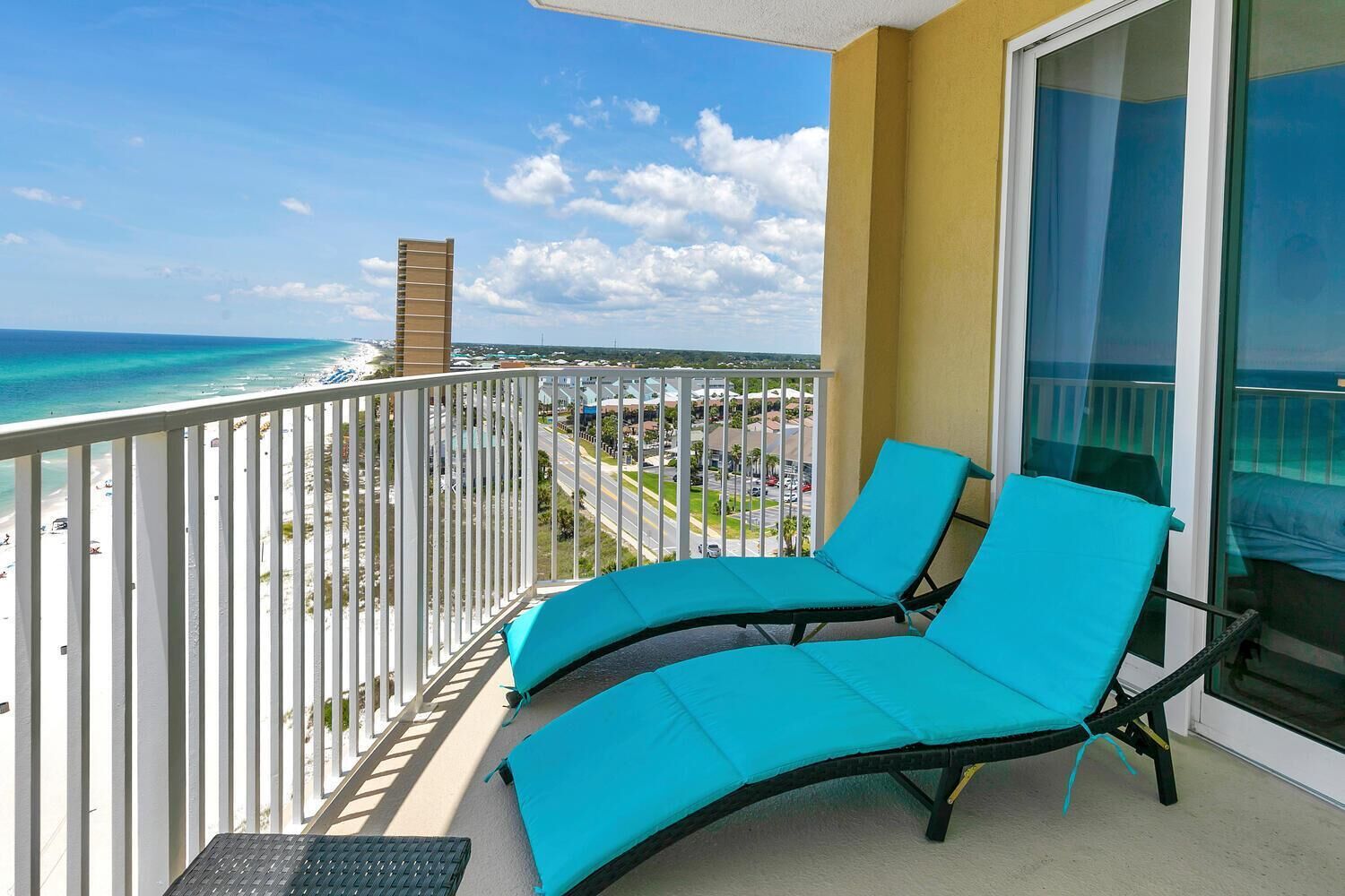 Un balcón con dos sillones azules, vista a la playa y cielo despejado.