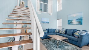 Un salon moderne avec un canapé bleu, un escalier en bois et une vue sur l’océan par la fenêtre.