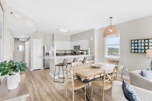 A modern kitchen with white cabinets, a central island, and a dining area with a wooden table and chairs. - Shores of Panama 431 (Panama City Beach)