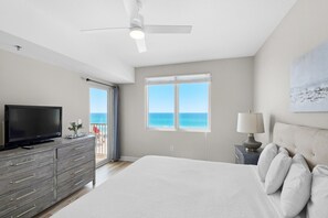 A bedroom with a bed, a TV, a ceiling fan, and a window with a view of the ocean. - Shores of Panama 431 (Panama City Beach)