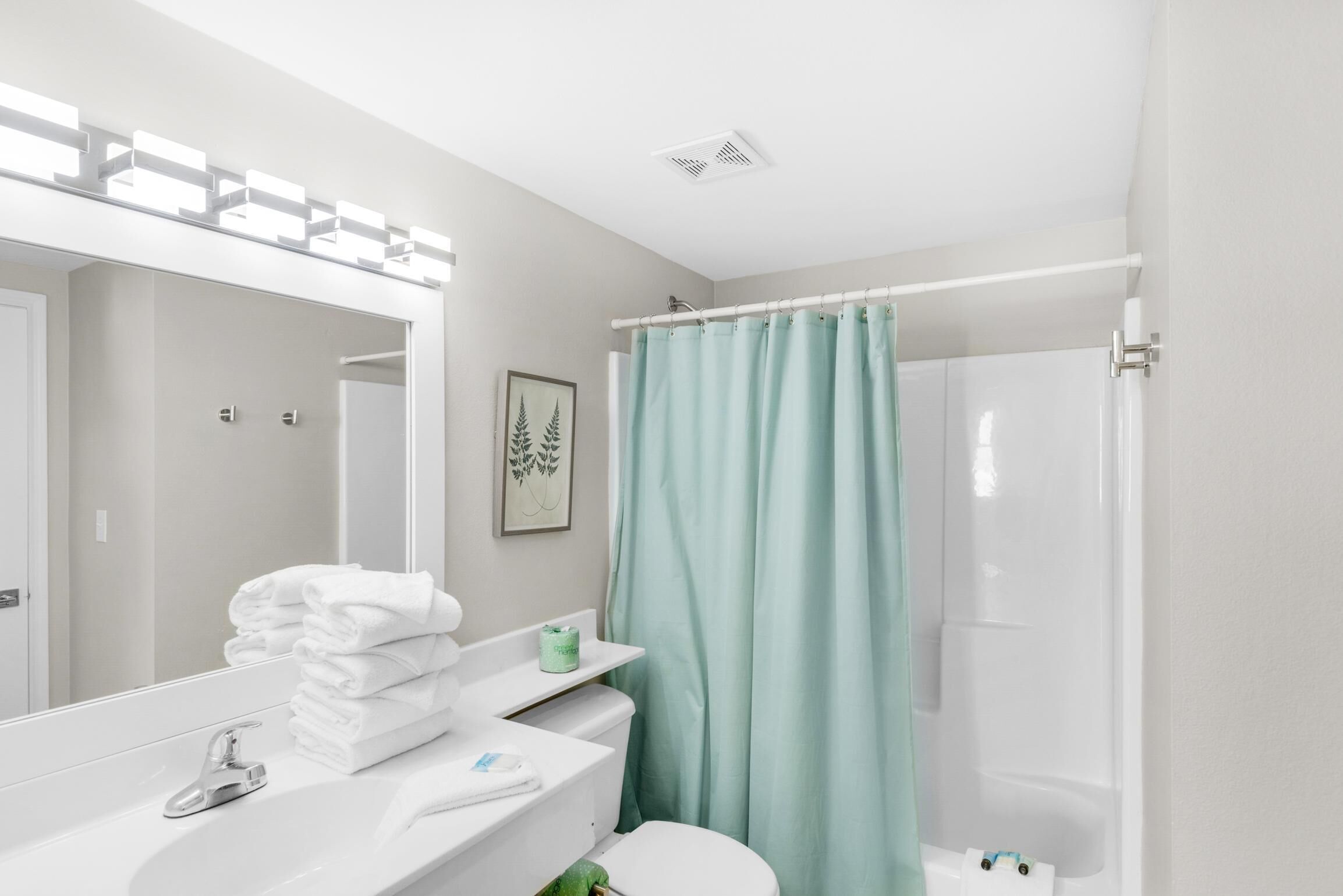 A modern bathroom with a white sink, a mirror, a toilet, and a shower curtain.