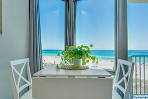 En balkon med et hvidt bord og stole, en potteplante og udsigt til stranden.