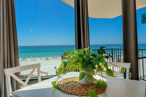 Een balkon met uitzicht op het strand, een tafeltje met een plant en een witte stoel.
