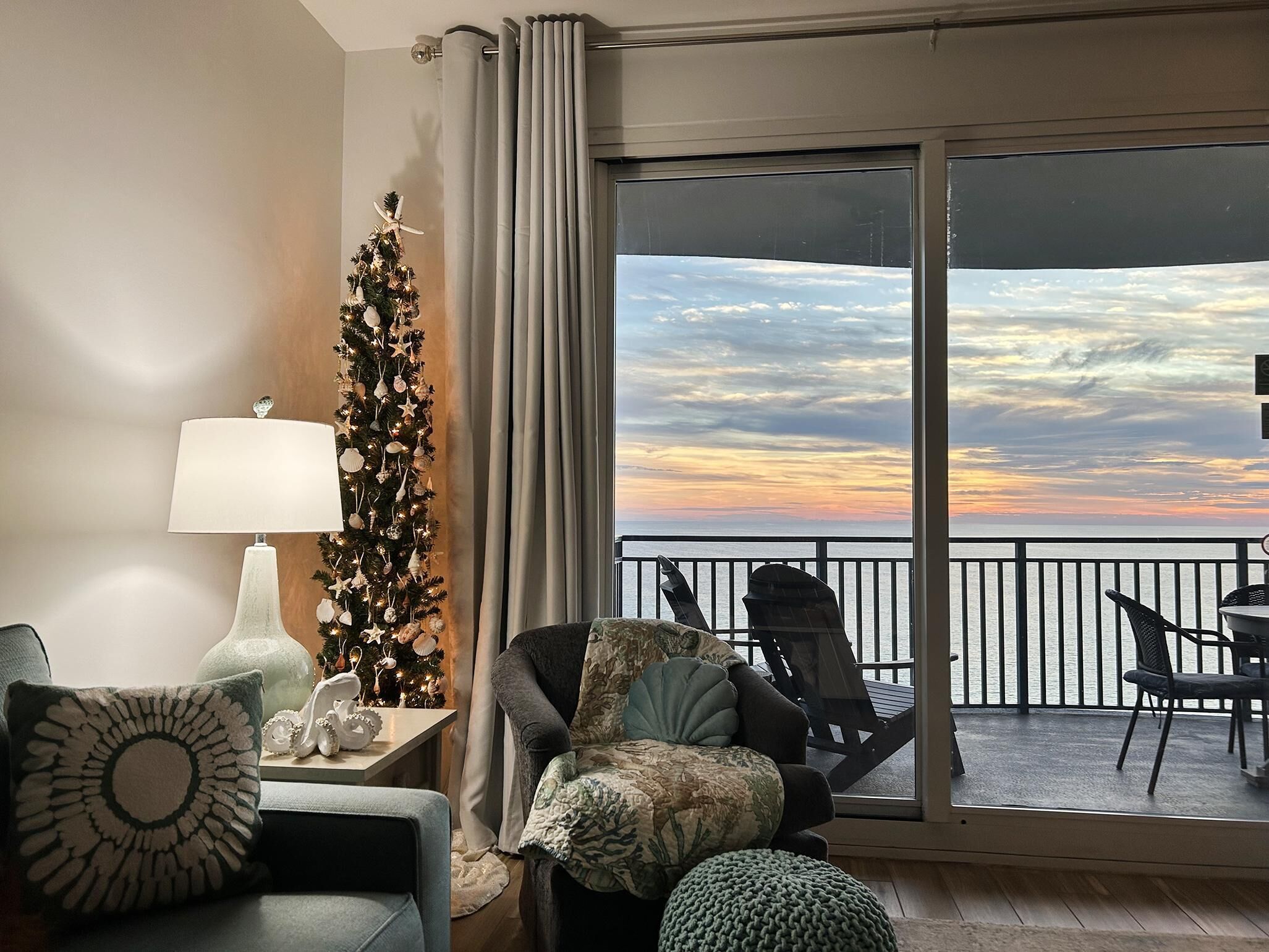 Ein gemütliches Wohnzimmer mit Weihnachtsbaum, Lampe und Blick auf den Sonnenuntergang über dem Wasser.