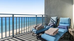 Un balcón con vista a la playa y al océano. Hay dos sillones de exterior con cojines y mantas.