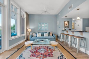 A modern living room with a blue sofa, a glass coffee table, and a colorful rug.