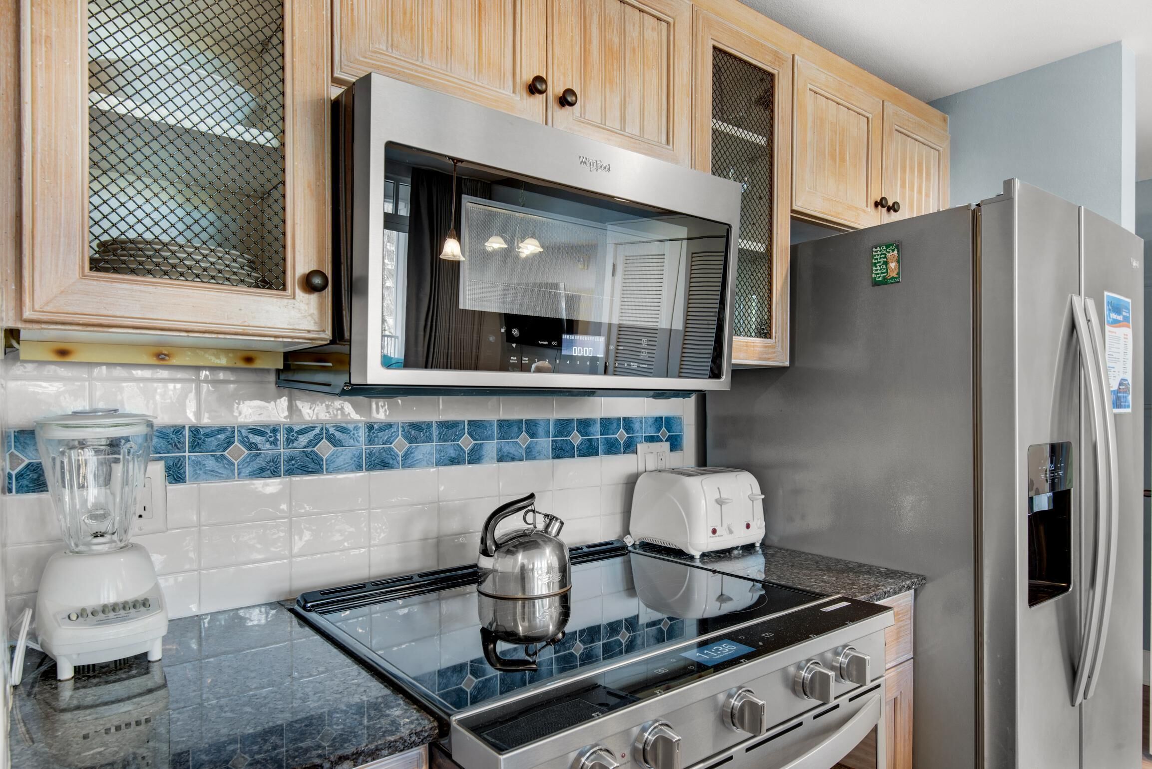 Een moderne keuken met houten kastjes, een roestvrijstalen koelkast, een inbouwoven, een gasfornuis, een blender en een waterkoker.