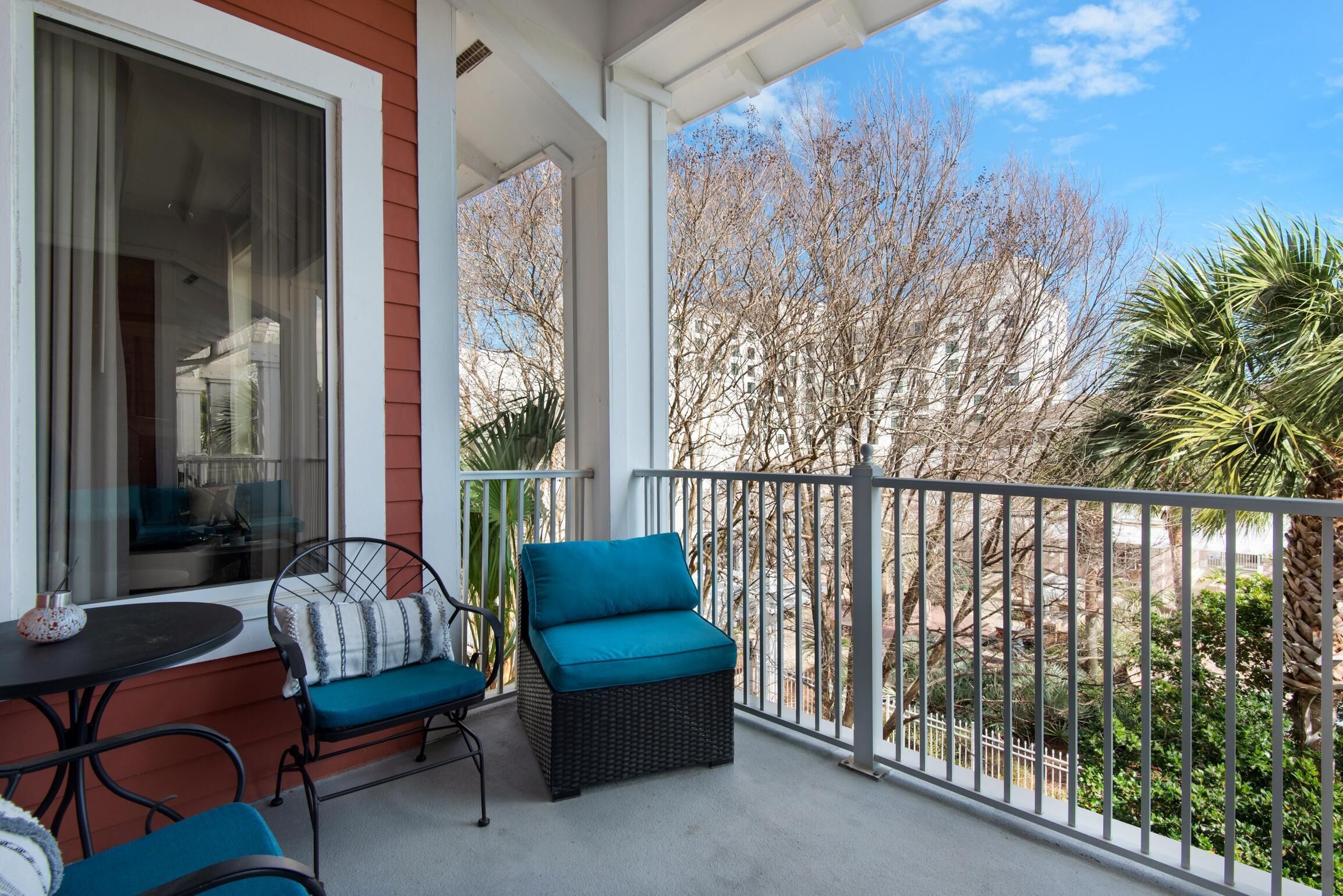 A balcony with wicker furniture, a table, and a view of trees and buildings.