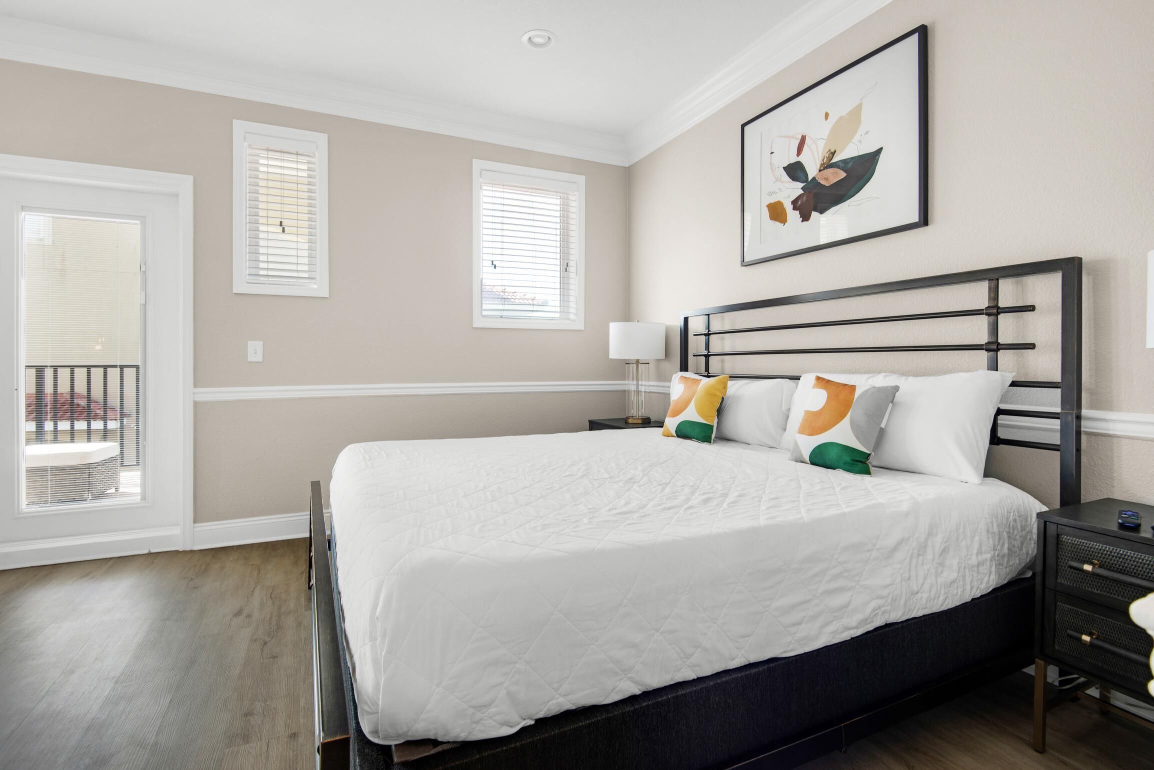 Une chambre à coucher avec un grand lit, une table de chevet, une lampe fixée au mur et une fenêtre avec des stores.