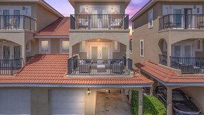 A multi-story residential building with a red-tiled roof, balconies with black railings, and a garage. - Bella Costa 160- Sandy Feet Retreat (Panama City Beach)