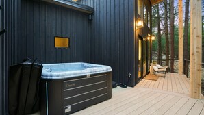 Un jacuzzi en una terraza de madera con un muro de madera oscura y puertas de cristal que dan a una zona de estar.