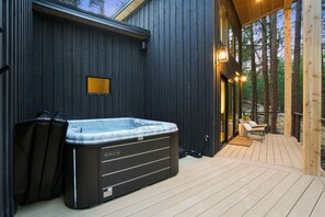 Una vasca idromassaggio su un pontile in legno, con un muro di legno scuro e porte in vetro che danno su una zona relax.