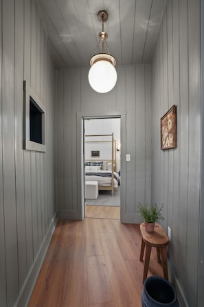 Un corridoio con pavimento in legno, un lampadario a soffitto, una porta che dà su una camera da letto e un piccolo tavolino con una pianta.