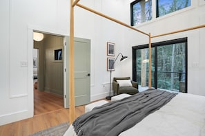 A bedroom with a large bed, a window with a view of trees, a chair, and a desk.