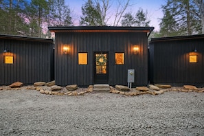 A rustic cabin with a front door, two windows on either side, and a small porch area with steps leading up to the door.