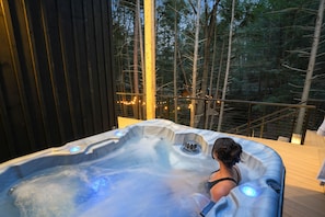 A hot tub with a wooden deck and a view of a forest.