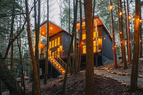 A modern cabin with a staircase leading to the upper level, surrounded by a forest.
