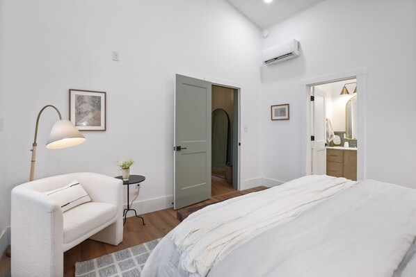 Ein Schlafzimmer mit einem Bett, einem Sessel, einer Lampe und einer Tür zu einem Badezimmer.