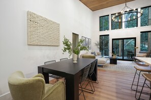 A modern interior with a dining area, seating, and large windows offering a view of the outdoors.