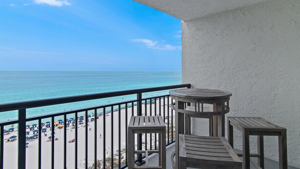 A balcony with a view of a beach and ocean. There are three wooden tables and a railing. - Sundestin 1008 (Destin)