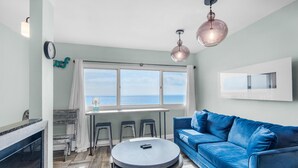 Ein Wohnzimmer mit einem blauen Sofa, einem runden Tisch und einem Fenster mit Blick aufs Meer.