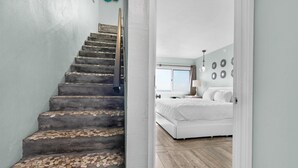 Eine Treppe führt zu einem Schlafzimmer mit einem Bett, einem Nachttisch und einem Fenster.
