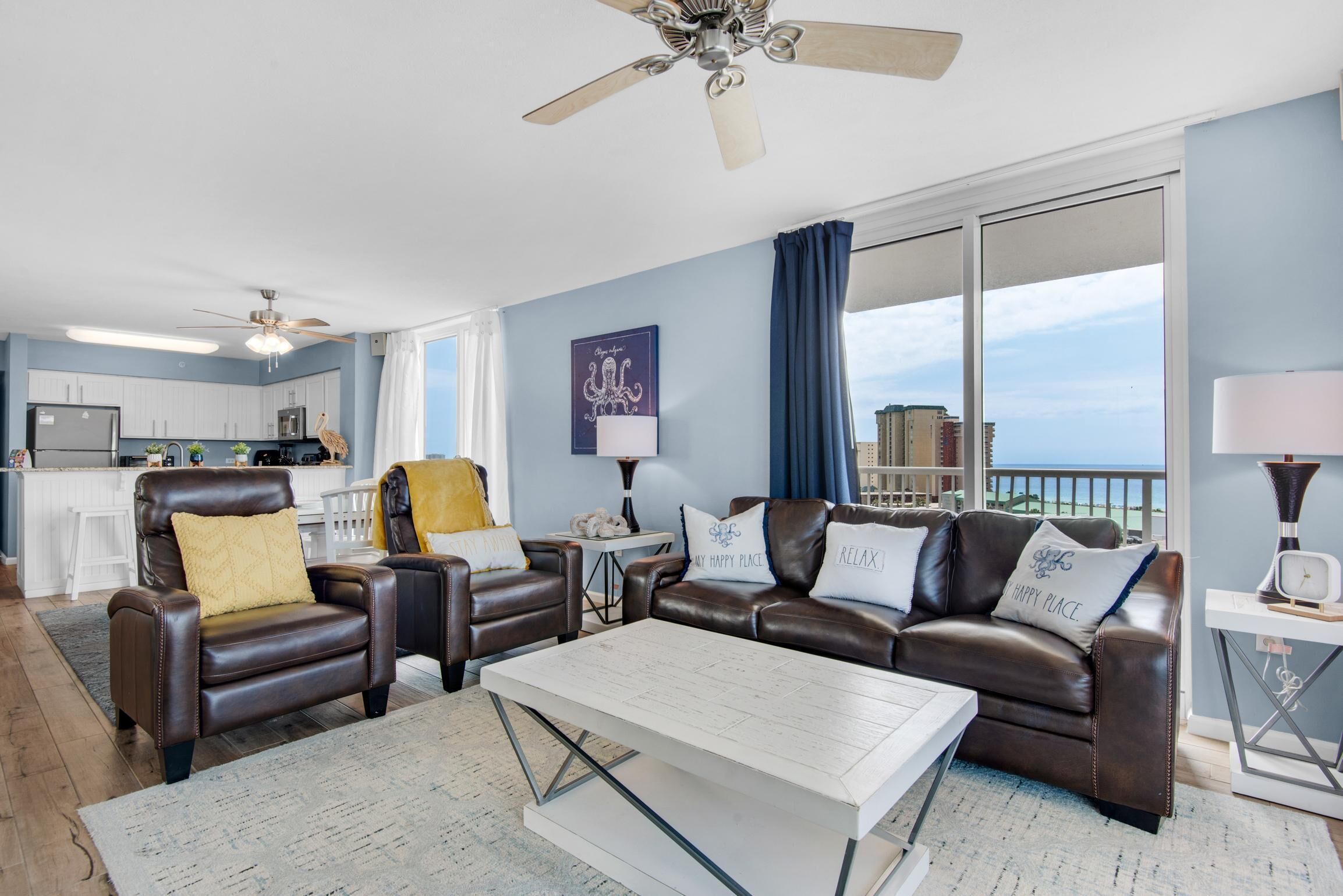 A modern living room with leather sofas, a white coffee table, and a ceiling fan.