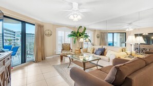A spacious living room with a sofa, coffee table, and armchairs, a balcony with a view of a building labeled "The Island," and a ceiling fan. - Inlet Reef 318 (Destin)