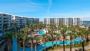 Ein Hotel mit mehreren Balkonen, einem zentral gelegenen Pool und Palmen.