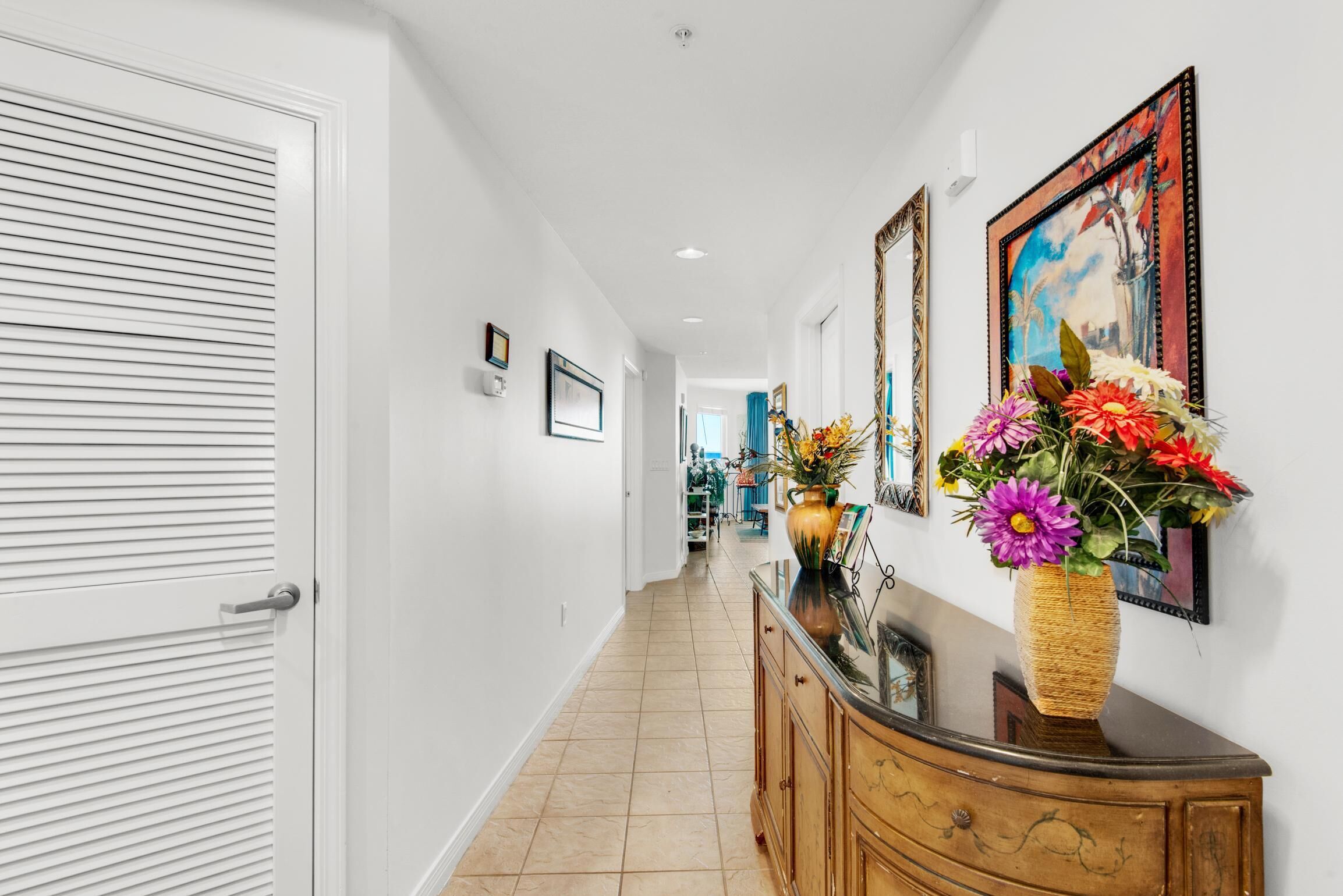 A hallway with a white door, a wooden cabinet with a vase of flowers, and framed artwork on the wall.
